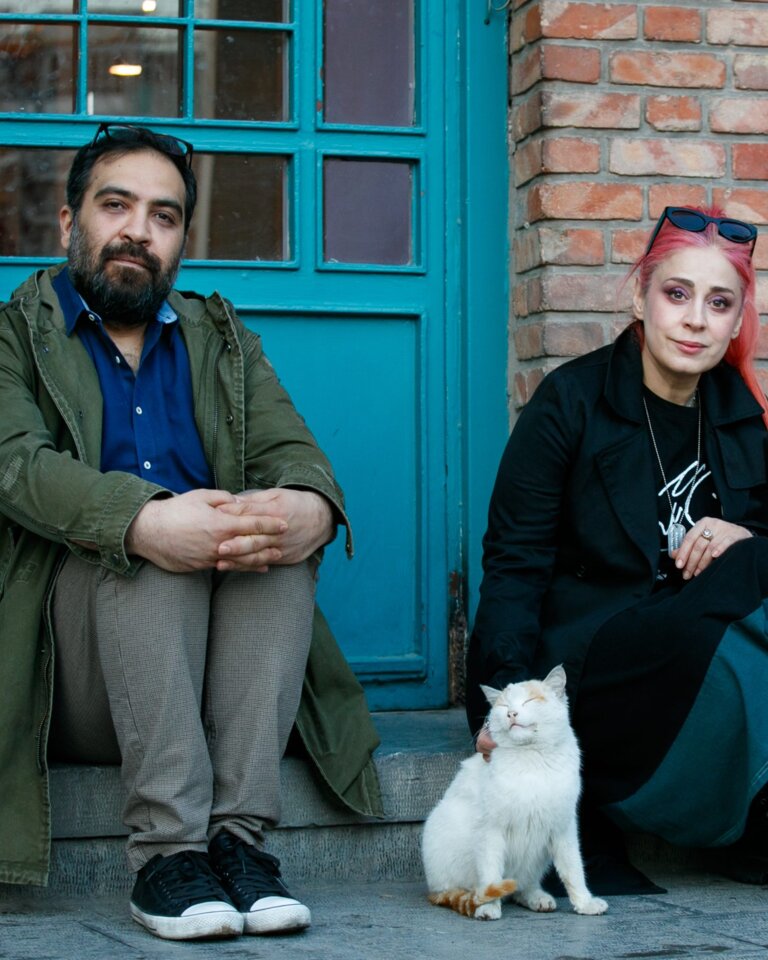 Das Foto zeigt einen Mann und eine Frau, die auf einer Stufe vor eine Tür sitzen. | © Behtash Sanaeeha und Maryam Moghadam |  Foto: Mehdi Hasani 